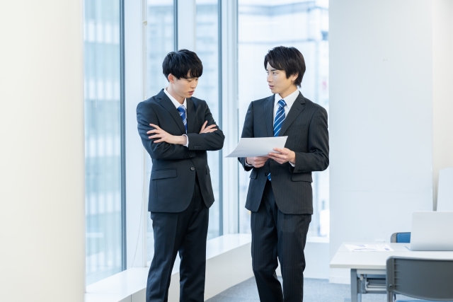 先輩社員が資料を見ながら、後輩社員にアドバイスをする様子